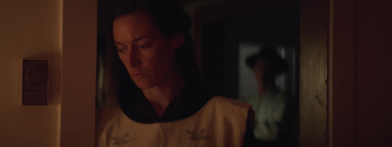 A man enters a house as a sad looking woman stands inside