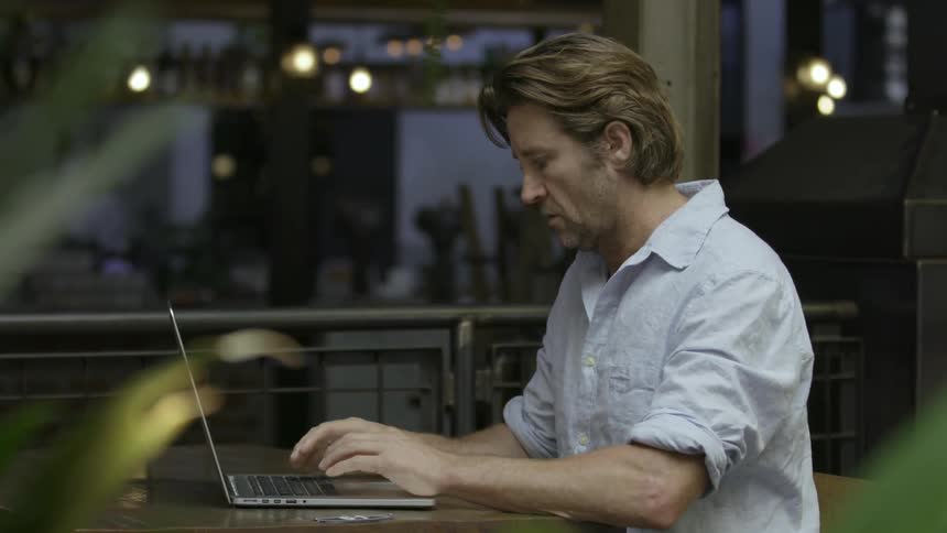 A man is sitting at a table typing on his laptop
