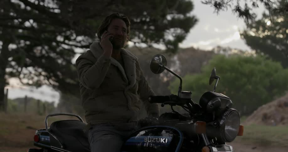 A man is sitting on his motorcycle talking on his cell phone