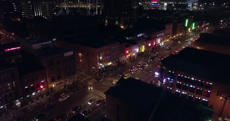 Vehicles travel down a street at night while a spotlight shines around the city