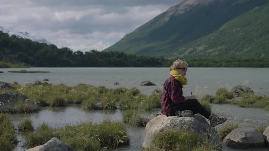 A woman sits on a rock in a lake