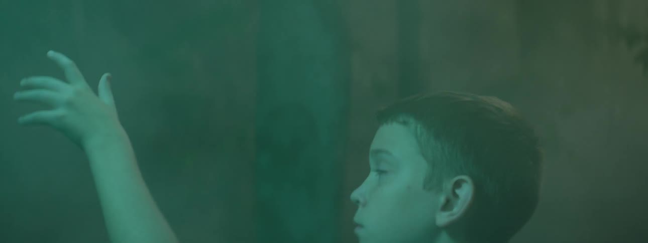 Child illuminated by green light waves hand on smoke
