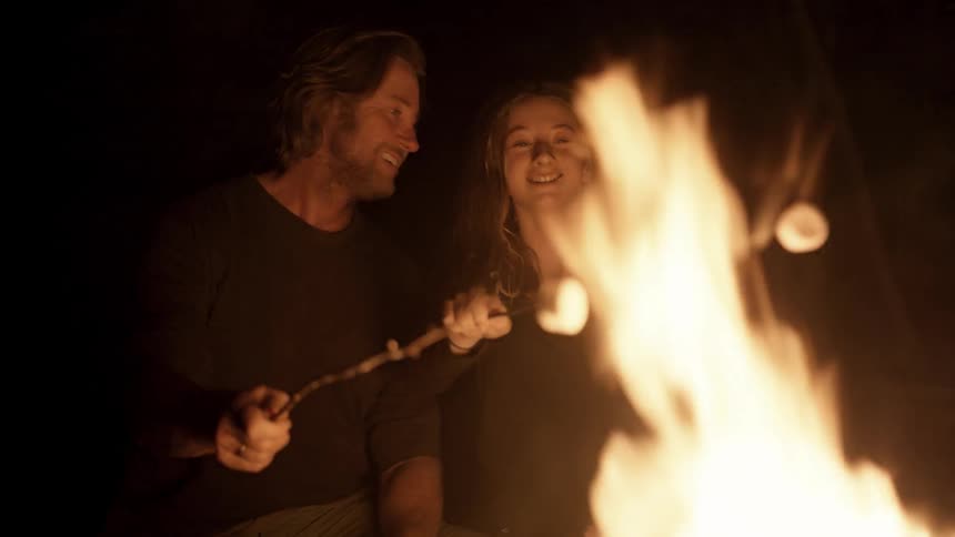 Man and girl roast marshmallows over a campfire at night