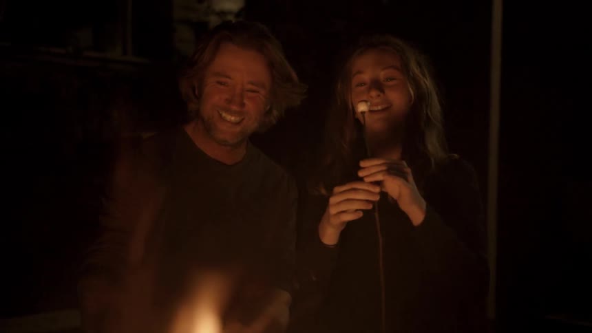 A man and a girl talking while cooking marshmallows over the fire