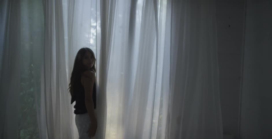 Young woman stands near white curtains, and looks back