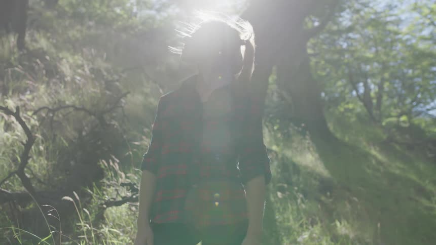 A woman standing on a hill looks up towards the sun