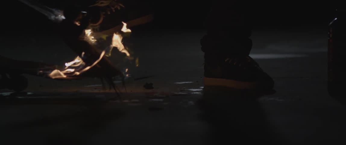 Someone is stepping on a broken skateboard thats on fire