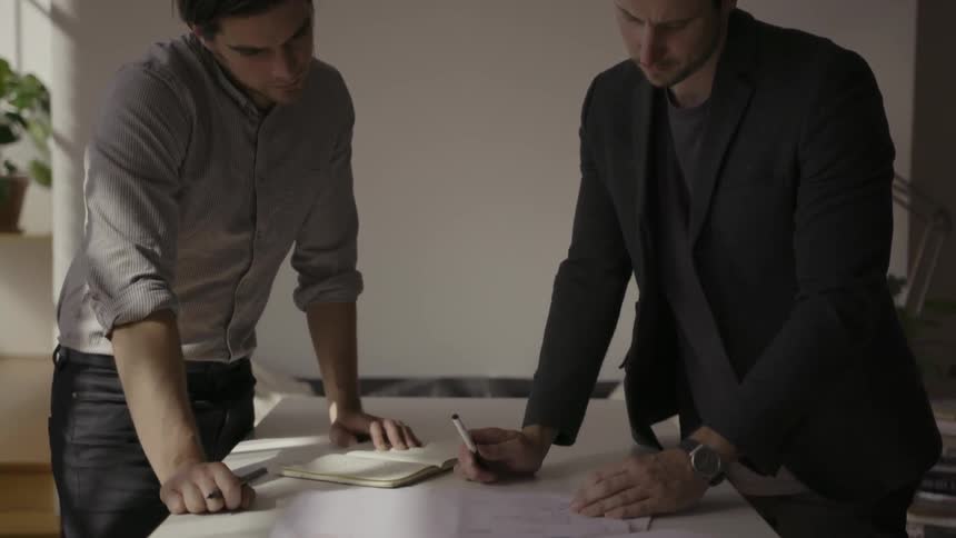 Two men are in an office looking at a piece of paper on the table