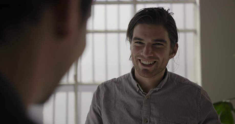 Two men smile and laugh while talking indoors