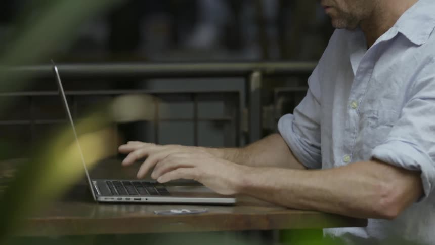 Man sits at a table and types on a laptop