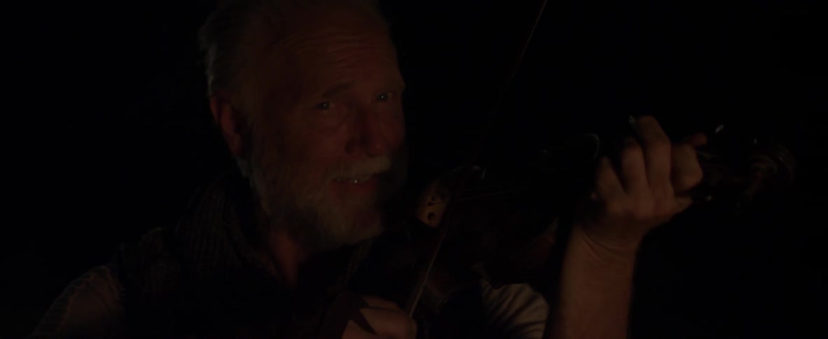 A man is playing the violin in the dark