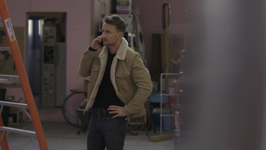 A man walks around a ladder talking on his phone