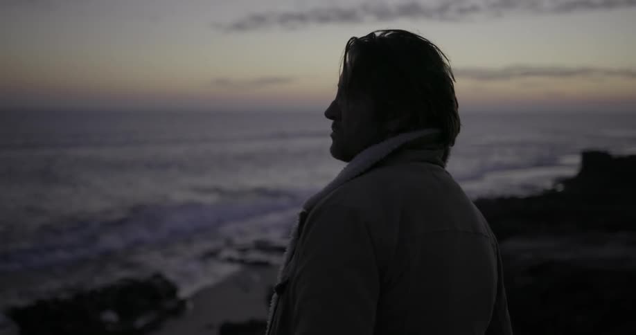 A man looks at the ocean at sunset