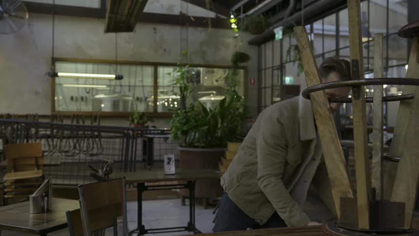 A man is pulling stools off of a table and putting them on the ground
