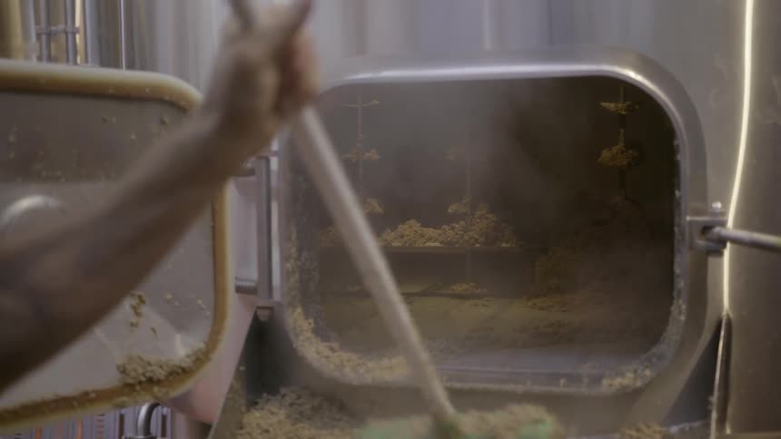 Man scrapes mush out of some machinery with a long handled mop