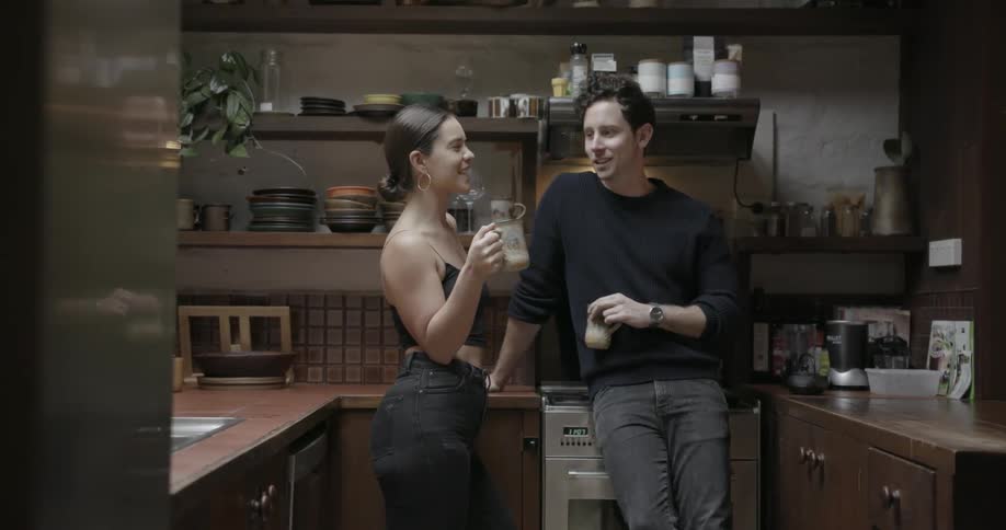 Man and woman talk in a kitchen while holding their drinks