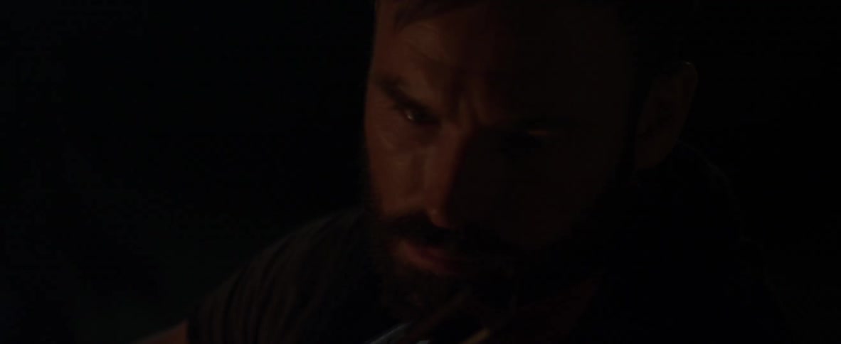 A bearded man plays the violin in a dark room