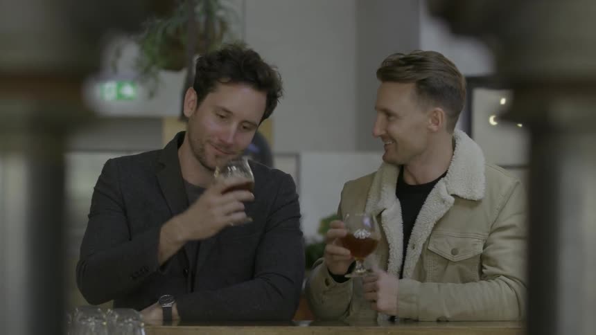 Two men raise glasses in a toast and drink