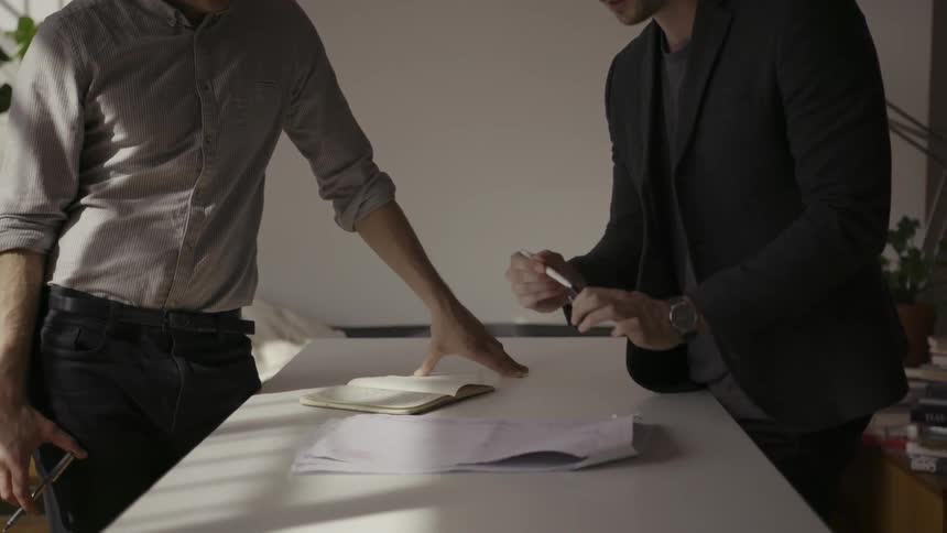 Two men look at a piece of paper and talk