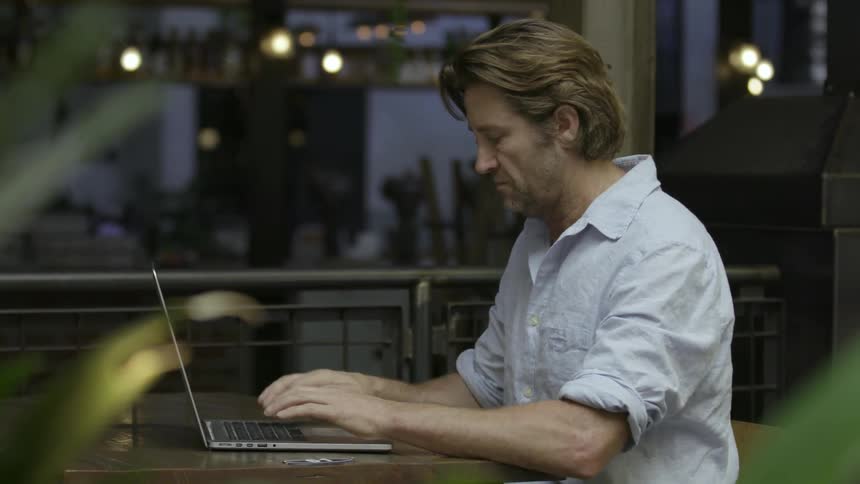 Man typing at a laptop calls out to a person walking by