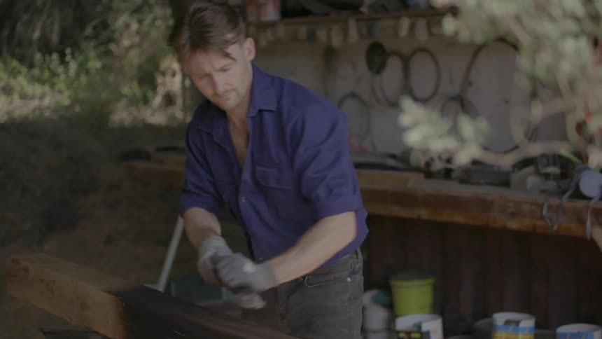 A man is shaving wood outside