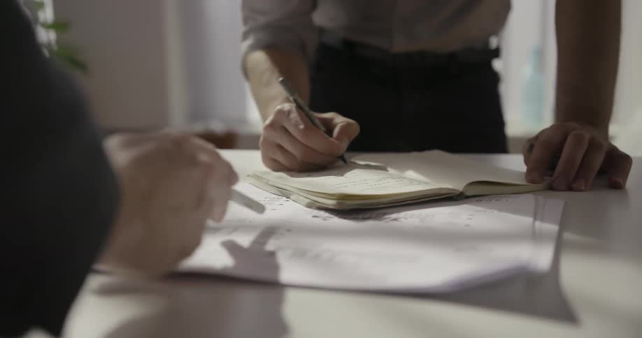 Two people write and point to paper on a desk