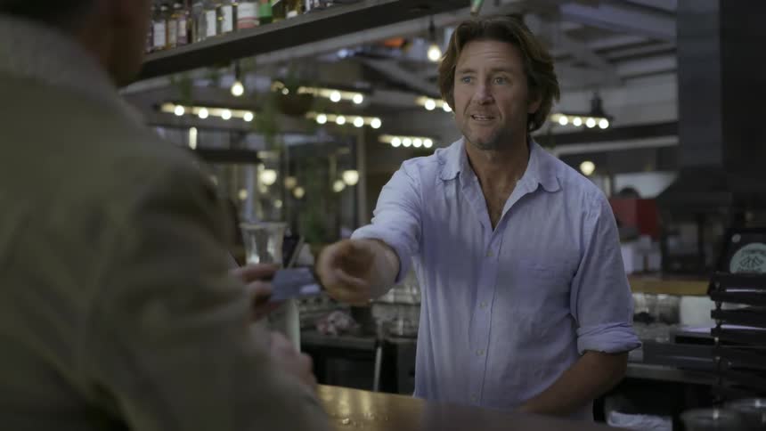 A bartender takes a credit card payment and chats with a patron