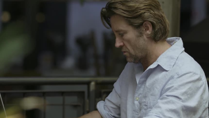 A man at a table is typing on a laptop