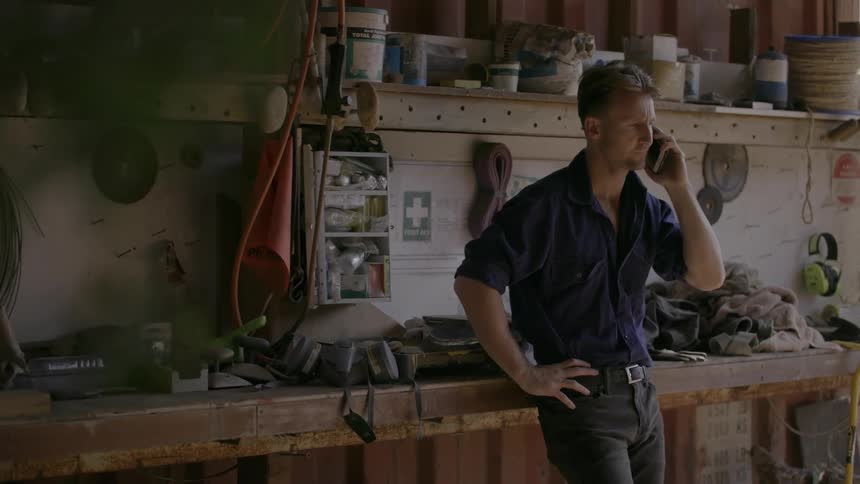 A man is standing in his workshop talking on a cell phone