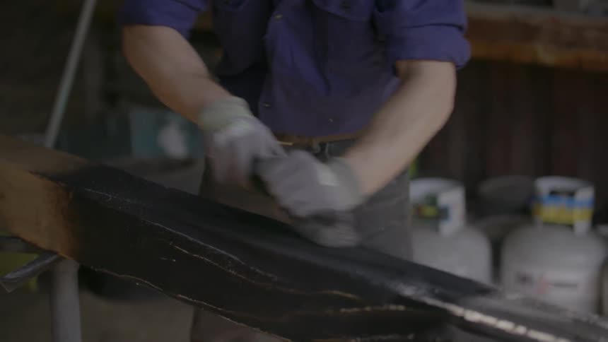 A man smoothes a wood beam in a workshop