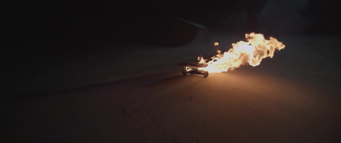 A man chases a burning skateboard in the dark