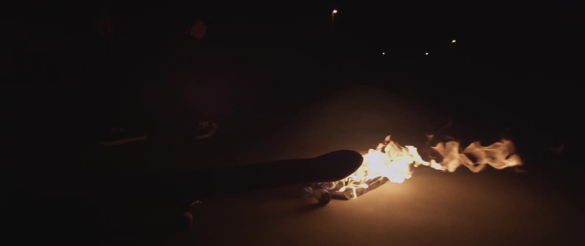 A fire blazes brightly at night off the end of a skateboard