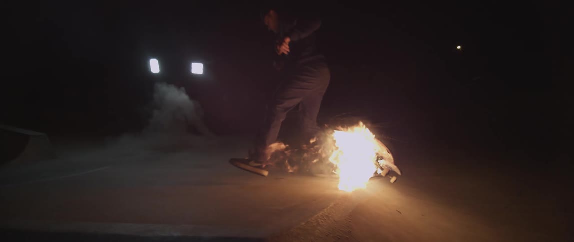 A person rides a skateboard that is on fire, and does a jump