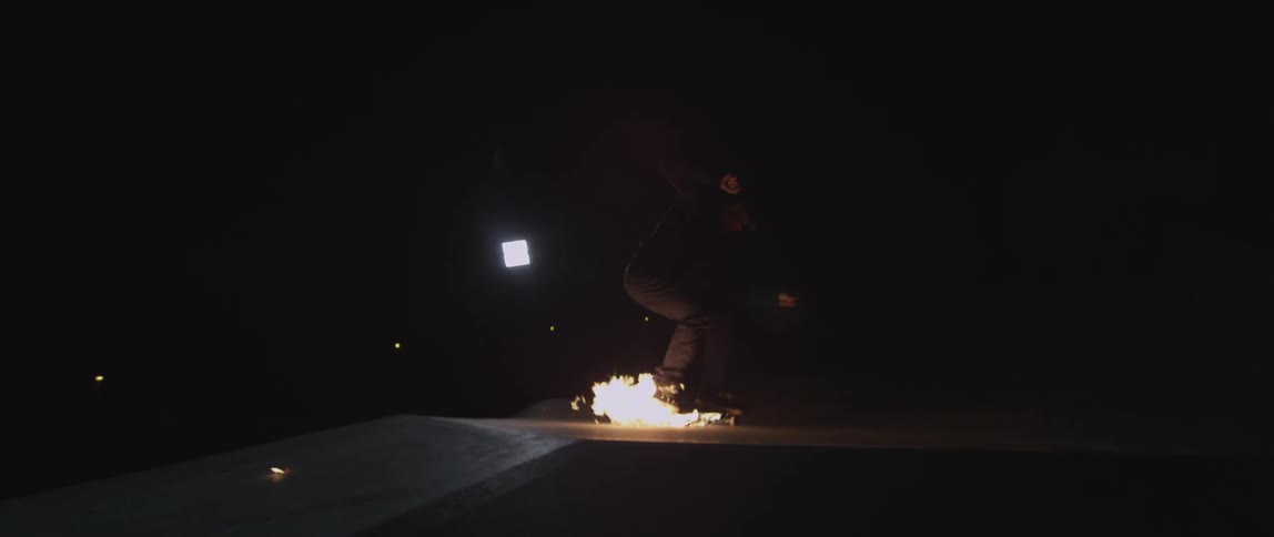 A man is riding a skateboard that is on fire at night