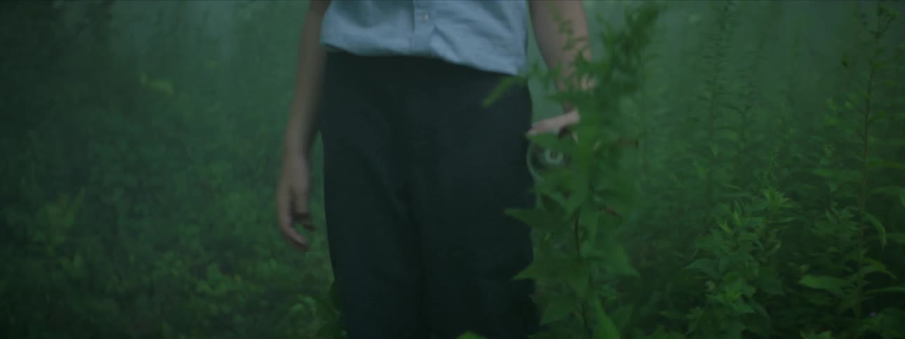 A boy holding a flashlight walks through the woods