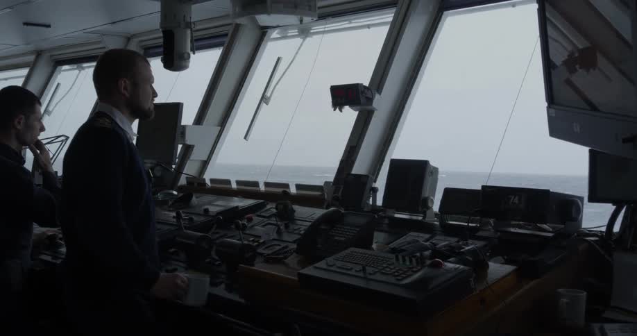 The captain looks out at the water through the windows of a ship