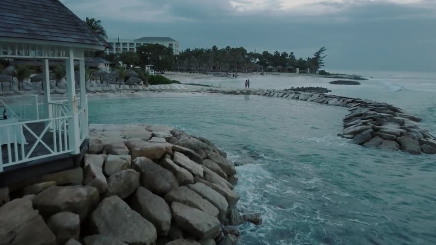Two people are filmed on some rocks next to the ocean