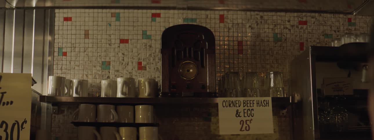 An old fashioned radio sits between coffee mugs and glasses on a shelf
