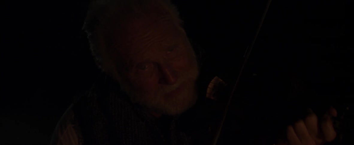 A man smiles as he plays the violin at night