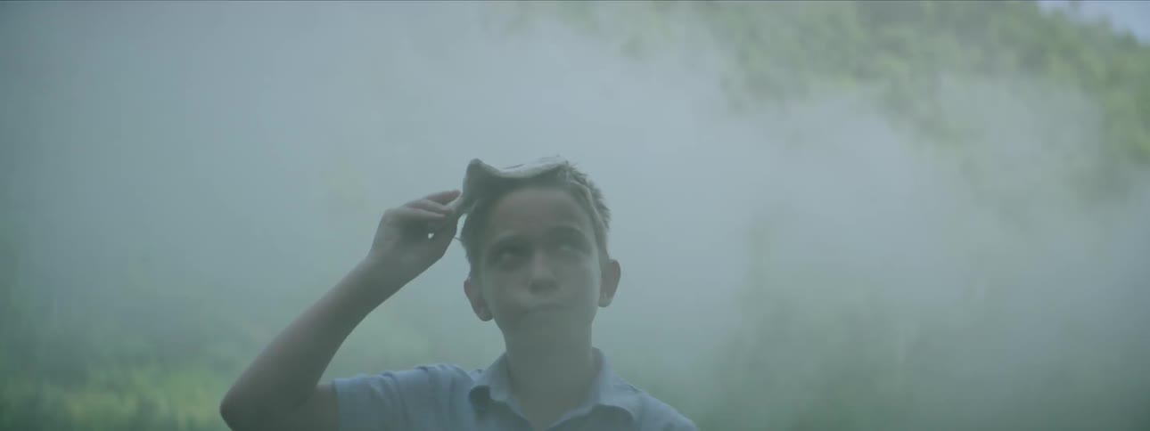 A boy walks through some smoke and removes his mask