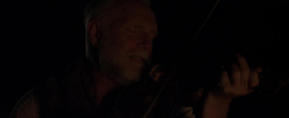 A man plays violin in a dark room