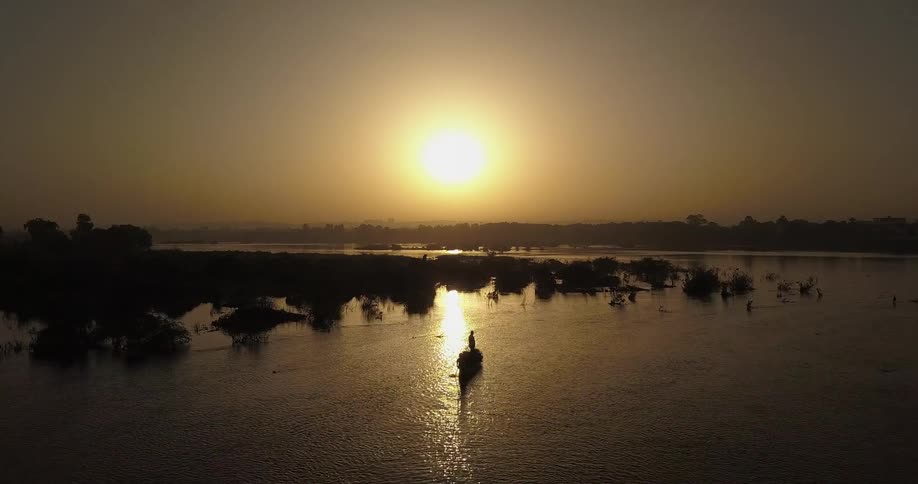 A person stands in a small boat on the water at sunset