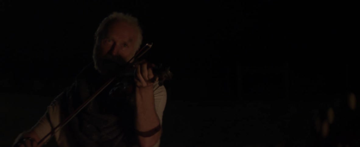 A man is playing the violin in the dark