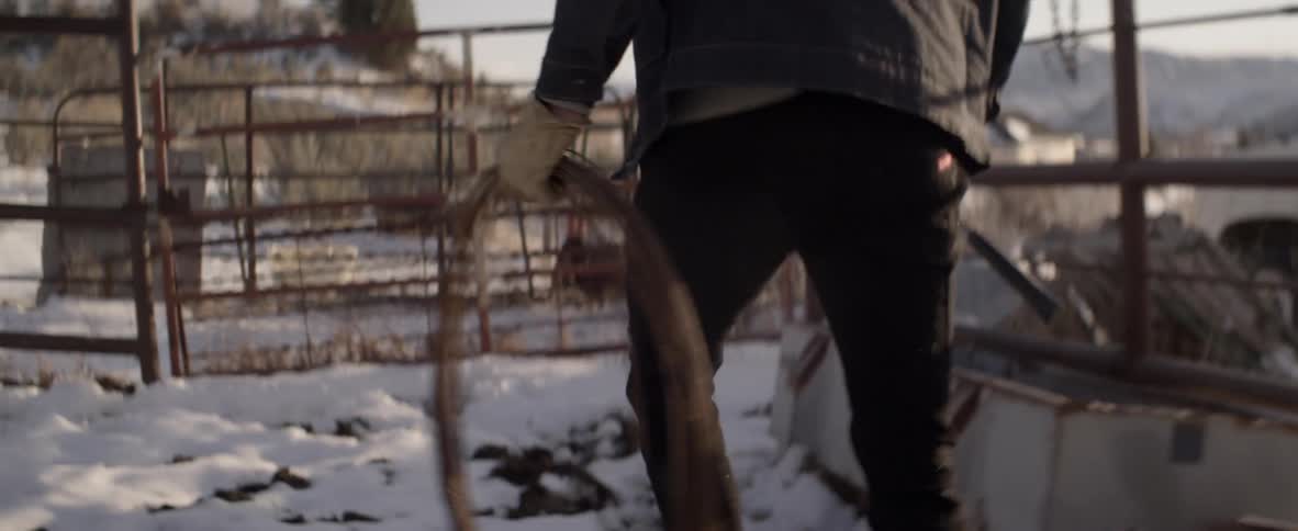 Someone walks in a snowy corral carrying rolled wire