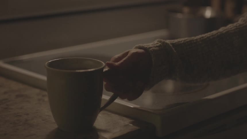 Person moving coffee mug from stove onto counter