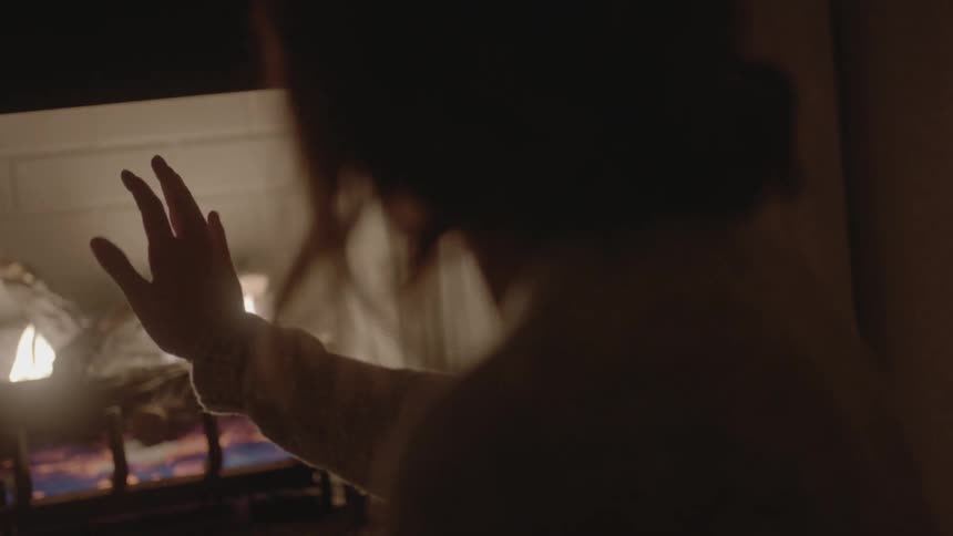 A woman holds her hand up to a burning fire in a fireplace