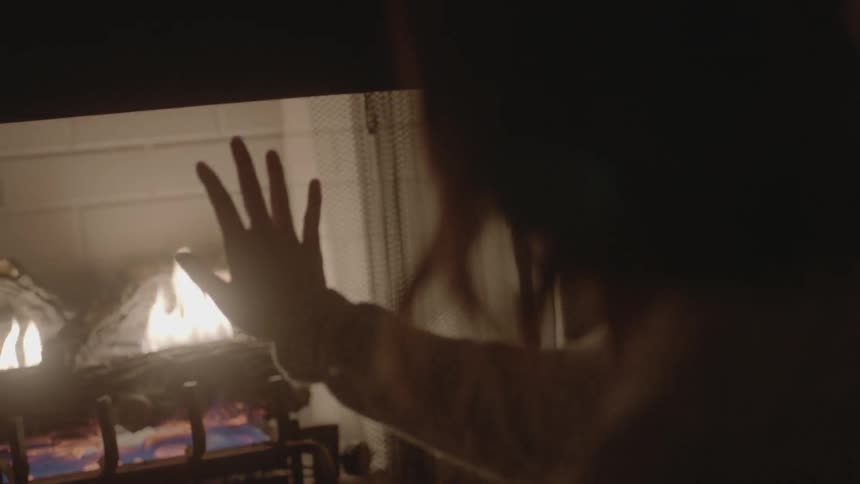 A woman holds up her hand to a burning fire in a fireplace