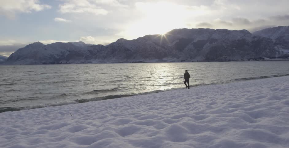 Man is walking on the sand while the water waves hit the shore