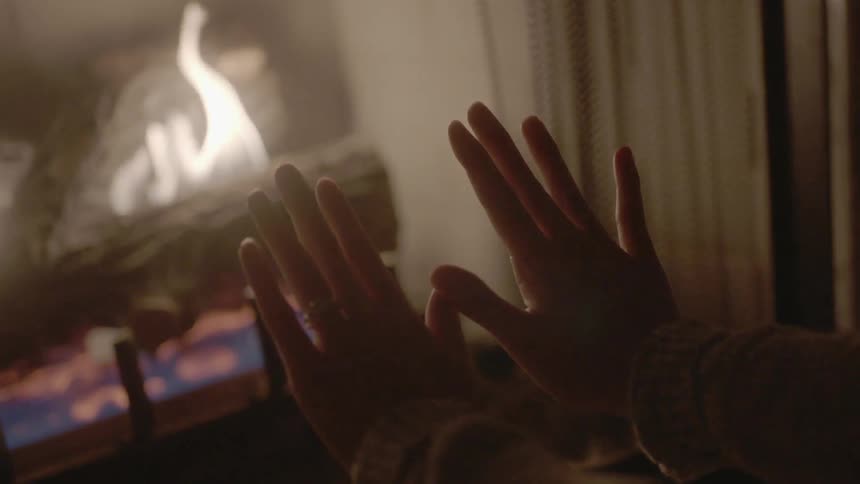 A woman places her hands near the fireplace for warmth