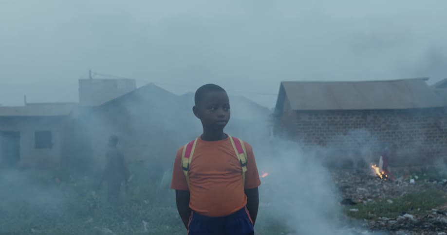Child standing in a village with fires burning and smoke billows